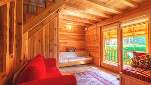 A wooden cabin interior with a bed, a red sofa, and a view through a glass door.