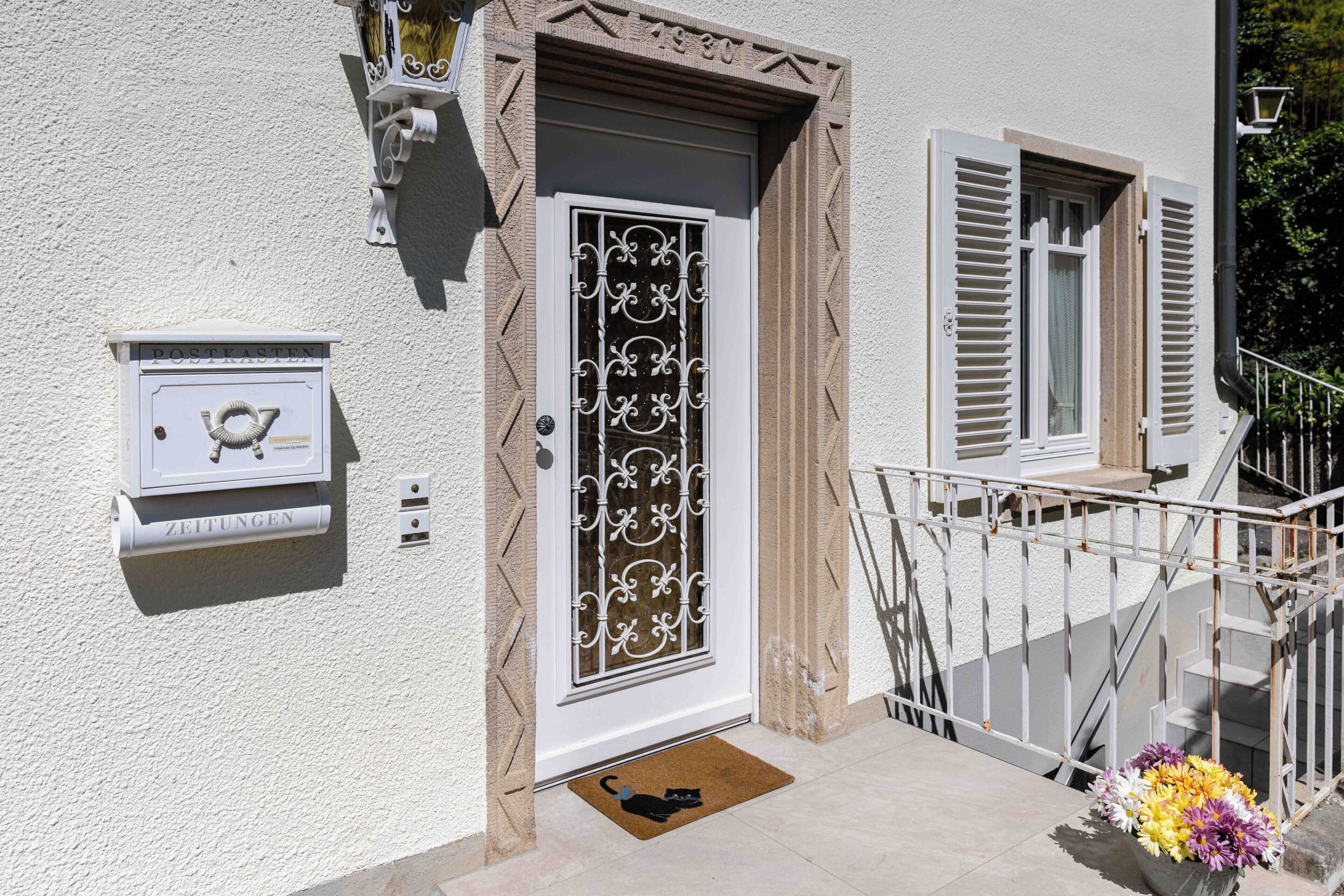 A building entrance with a mailbox, a decorative door, and a flower arrangement.