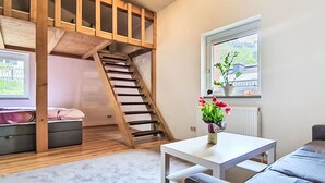 A room with a wooden staircase, a white table, a grey sofa, a window with a view, and a potted plant. - Apartment Maria by Interhome (Kaprun)