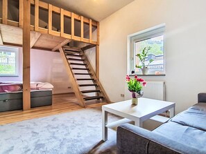 Una habitación con escalera de madera, una mesa blanca, un sofá gris, un ventanal con vistas y una planta en maceta.