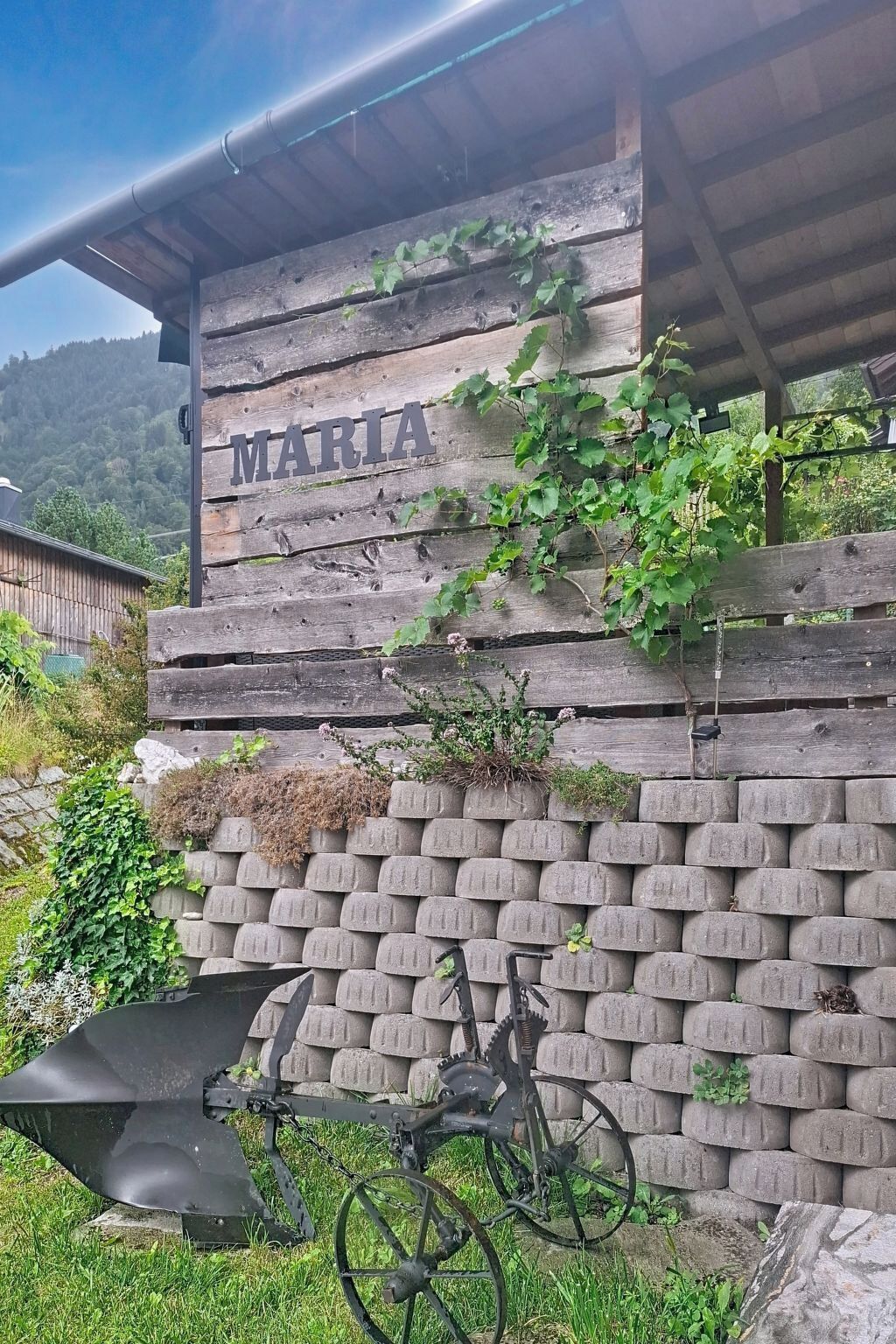 Pared de madera rústica con el nombre 'MARIA' y una bicicleta estacionada adelante.
