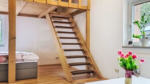 A wooden staircase leading to a loft bedroom with a bed, a small table with a vase of flowers, and a window with a plant. - Apartment Maria by Interhome (Kaprun)
