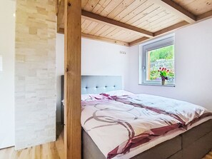 Un dormitorio con cama, ventana con vista a la vegetación y techo de madera.
