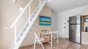 A modern kitchen with a stainless steel refrigerator, a wooden dining table with chairs, and a white staircase. - Charming 1BR in Pueblo Mijitas with Terrace by Mijas Golf (Mijas)