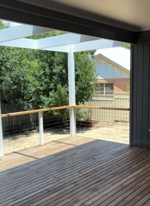 Eine Holzterrasse mit weißer Geländer, Blick auf einen Hinterhof mit Bäumen und einem Haus.