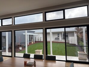 Ein Zimmer mit großen Fenstern, einem Holztisch und Blick auf ein Haus und eine Rasenfläche.