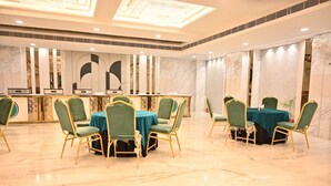 A hotel dining area with marble flooring, green upholstered chairs, and tables with teal tablecloths. - Hotel Velvet The Ultimate (Prayagraj)