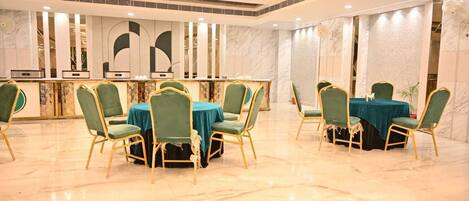A hotel dining area with marble flooring, green upholstered chairs, and tables with teal tablecloths.