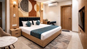 A modern hotel room with a large bed, bedside tables, a desk, a chair, a TV, and an air conditioning unit. - Hotel Velvet The Ultimate (Prayagraj)
