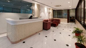 A modern reception area with a white reception desk, red seating, and a glass wall. - Hotel Velvet The Ultimate (Prayagraj)