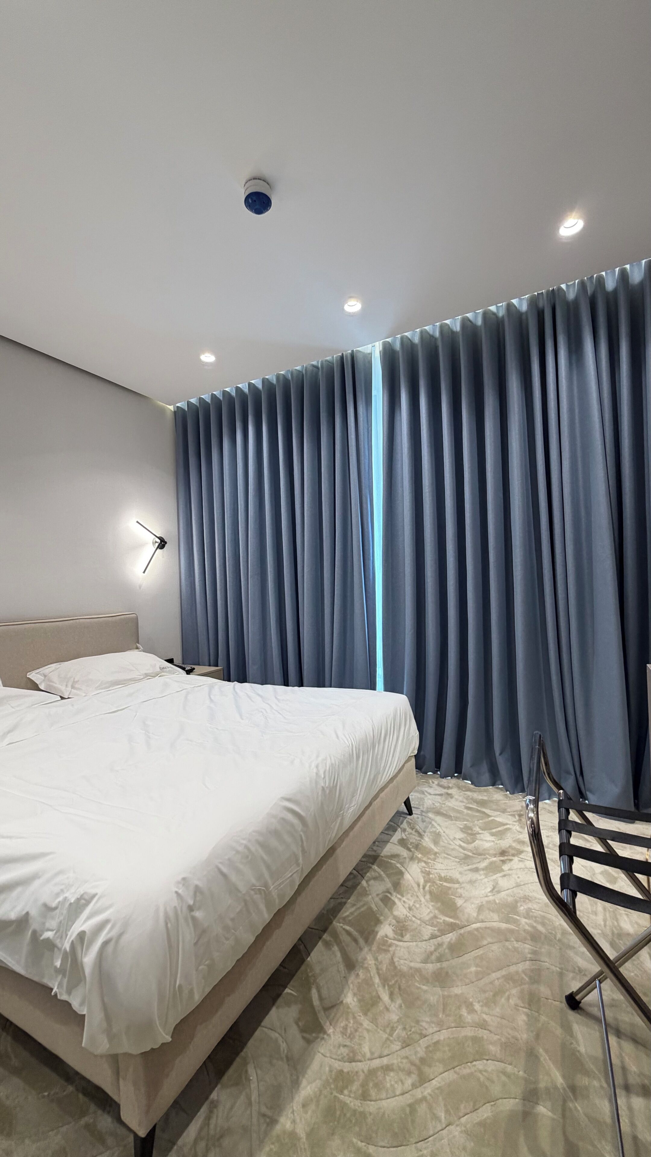 Ein modernes Hotelzimmer mit einem großen Bett, einem Nachttisch, einem Sessel und einer Wandlampe.