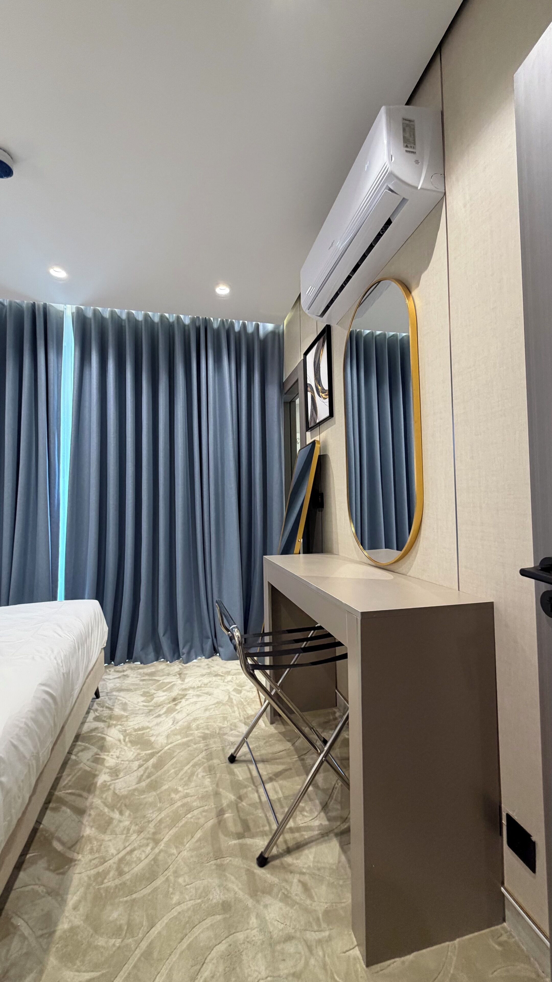Una habitación de hotel con cama, aire acondicionado, escritorio con espejo y una silla.