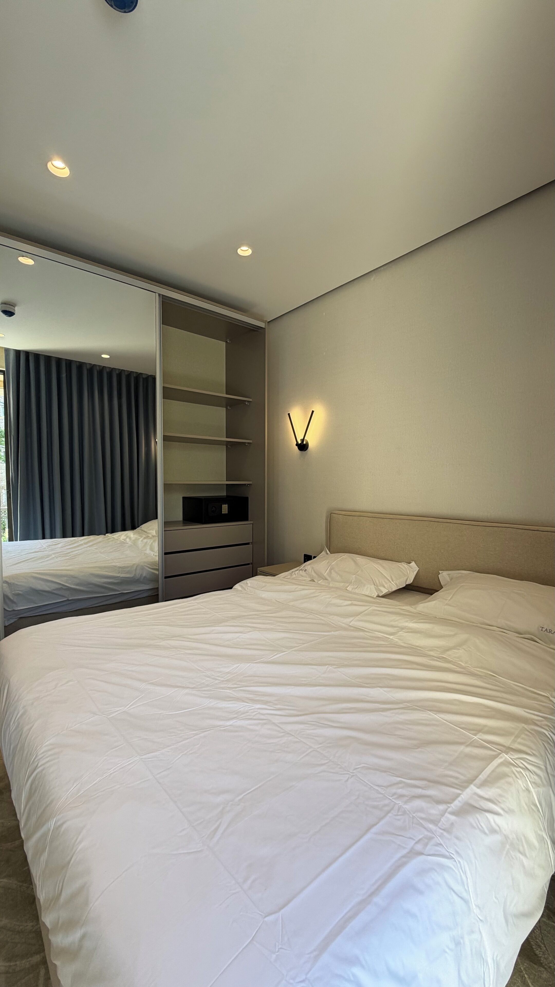 A modern bedroom with a large bed, built-in wardrobe, and a wall-mounted light fixture.