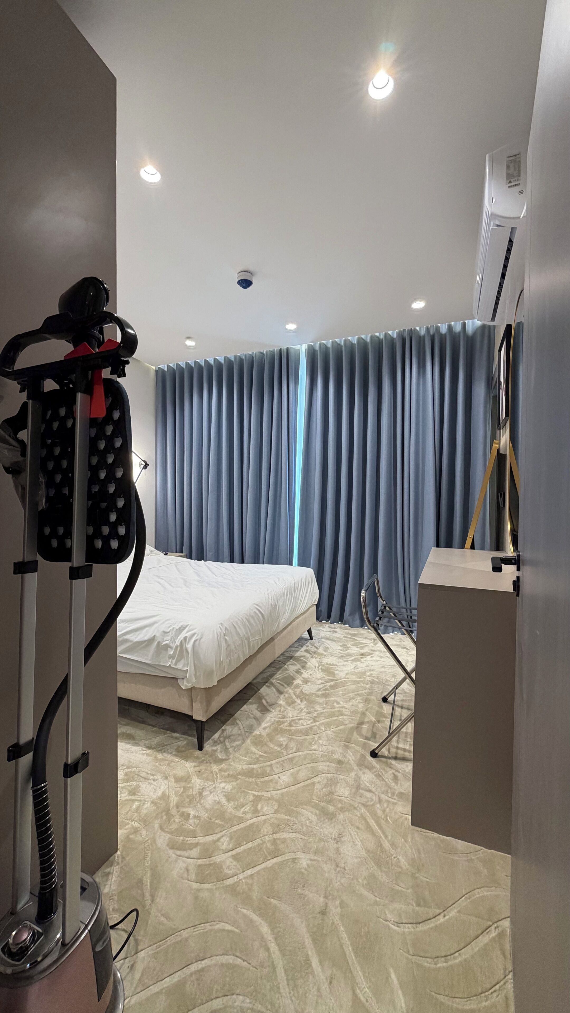 Ein Hotelzimmer mit Bett, Vorhängen, einer Decken-Klimaanlage und einem Staubsauger.