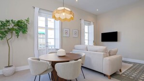 A modern living room with a round dining table, white chairs, a sofa, a television mounted on the wall, and a potted plant. - Bright Apartment in Granada Center San Anton 301 (Granada)