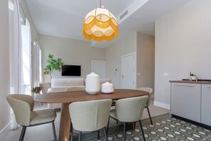 A dining area with a wooden table, four chairs, a hanging lamp, a sofa, a TV, and a kitchen area with cabinets. - Bright Apt in the Heart of Granada San Anton 304 (Granada)