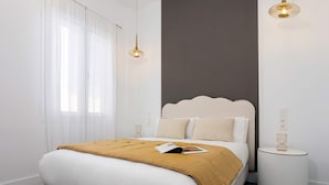 Un dormitorio con cama, mesitas de noche y una ventana con cortinas translúcidas.