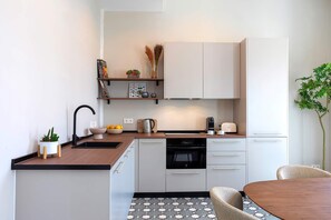 Een moderne keuken met witte kasten, een houten aanrechtblad, een inbouwoven en een eethoek met een ronde tafel en stoelen.