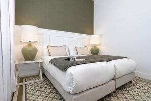 A neatly made bed with a grey blanket, two bedside lamps, and a patterned floor. - Luxurious 3 bd Apartment in Granada San Anton 302 (Granada)