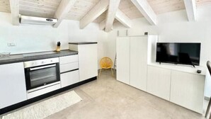 Una cucina moderna con mobili bianchi, forno integrato, piano di lavoro nero e televisore a schermo piatto montato a parete.