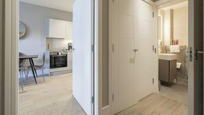A modern kitchen with white cabinets and a dining area with a table and chairs. - Superb 2 Bedroom Apartments (London)