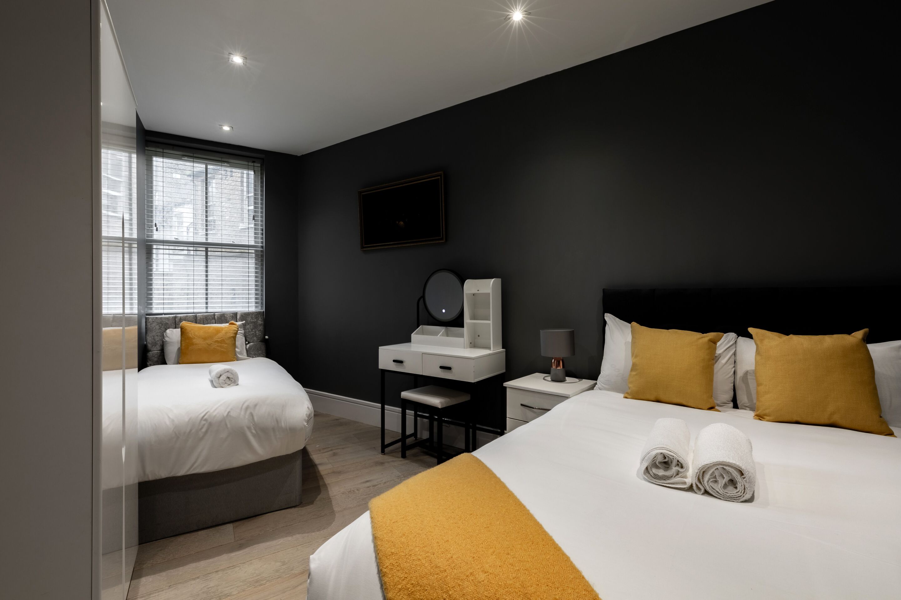 A modern hotel room with two beds, a desk, a vanity, and a large window.