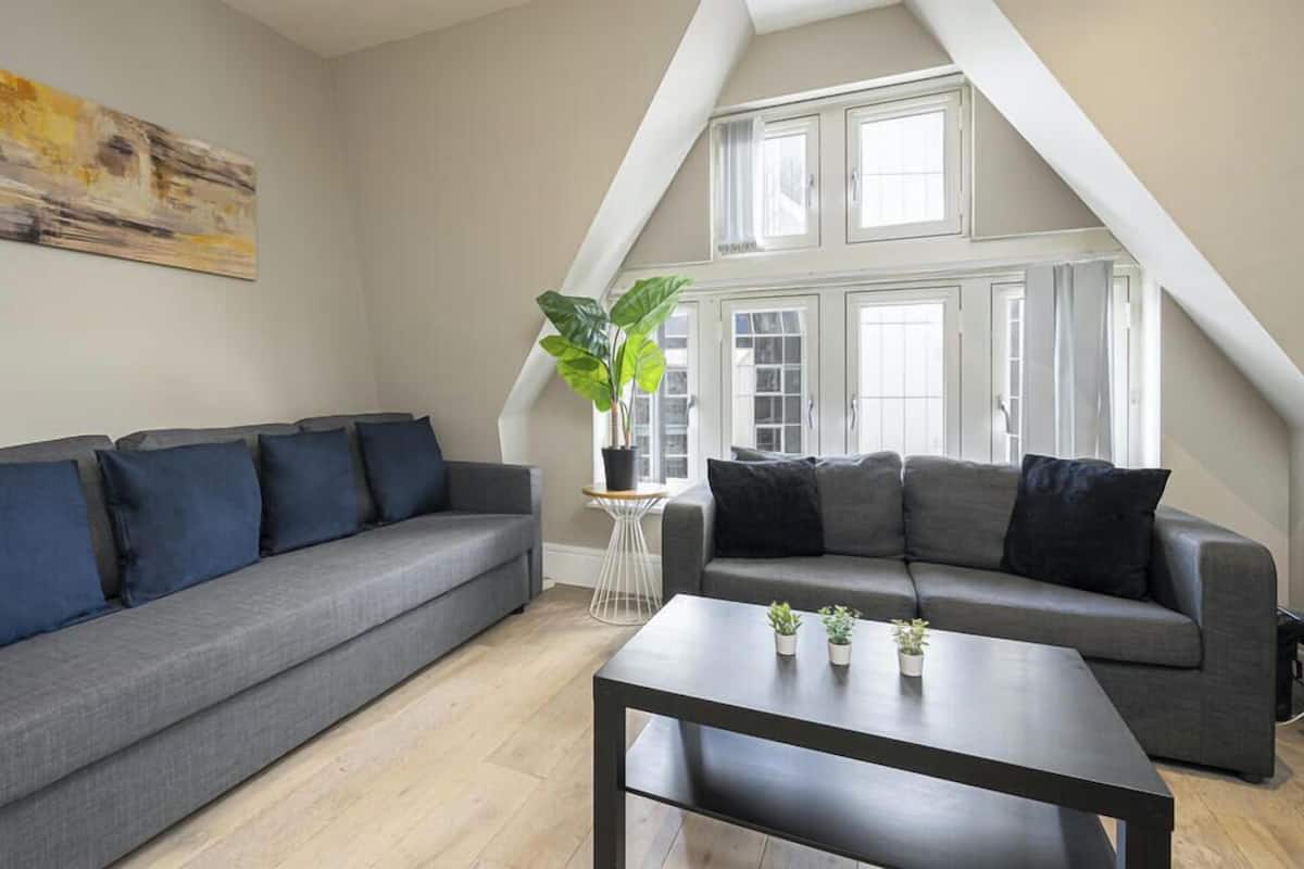A living room with two grey sofas, a coffee table, and a large window with curtains.