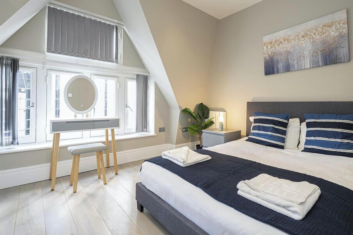 A bedroom with a bed, bedside table, lamp, and a large window with curtains.