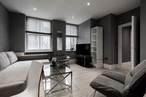 Una sala moderna con sofá, sillón, mesa de centro de vidrio y televisión.