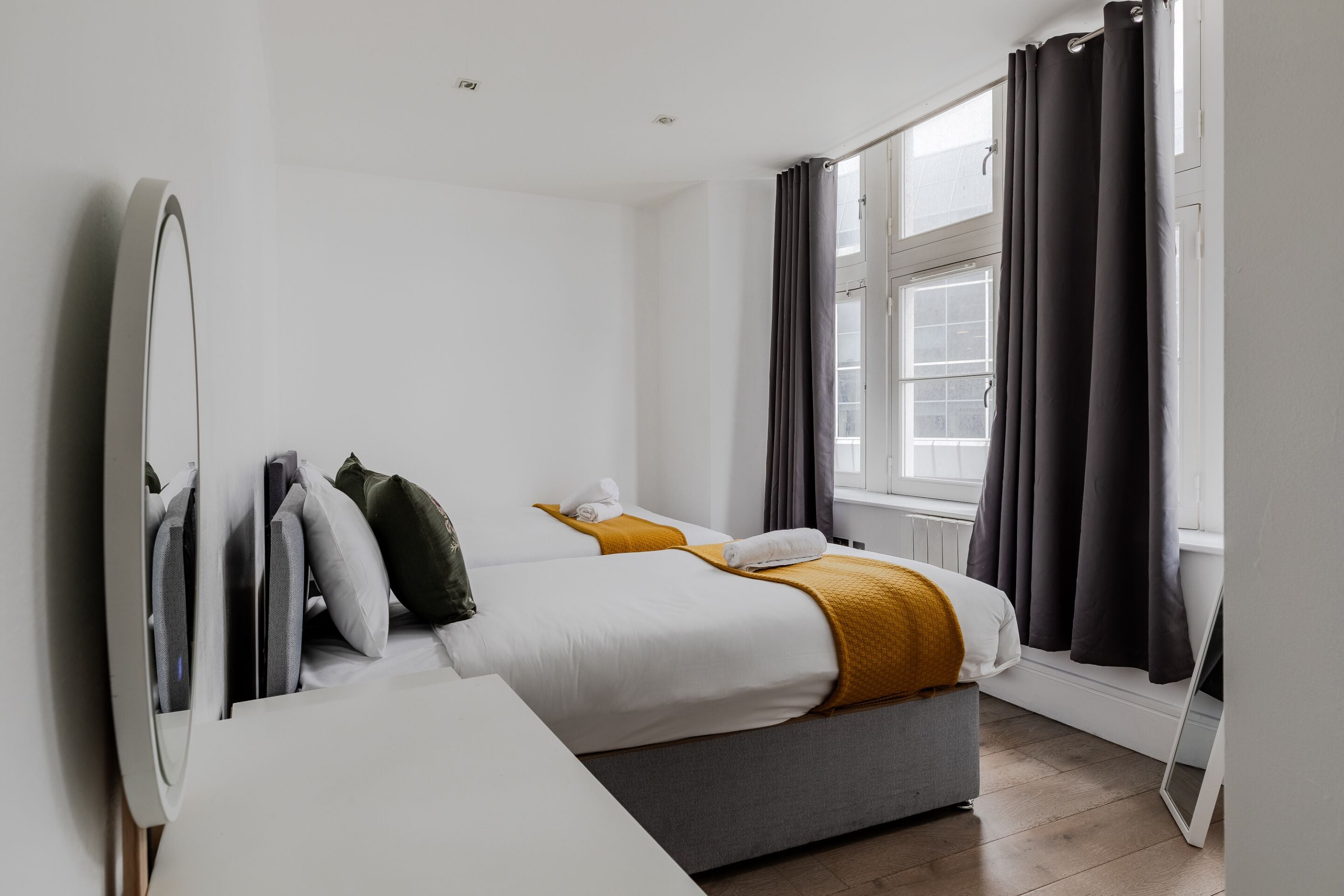 Een hotelkamer met een bed, nachtkastje, spiegel en raam met gordijnen.