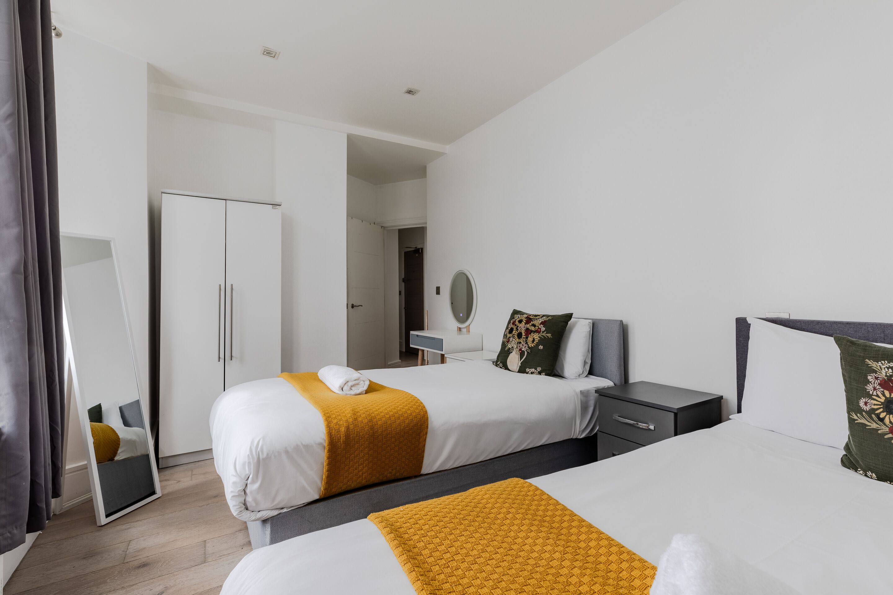 A hotel room with two beds, a wardrobe, a mirror, a bedside table, and a nightstand.