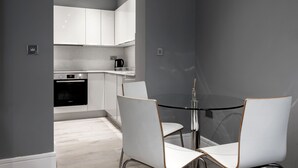 A modern kitchen with white cabinets, a black oven, and a glass table with two white chairs. - Superb 2 Bedroom Apartments (London)