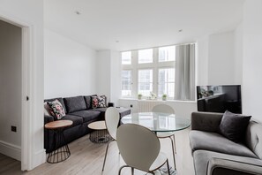 Una sala de estar moderna con un sofá gris, una mesa de comedor de vidrio y un televisor montado en la pared.