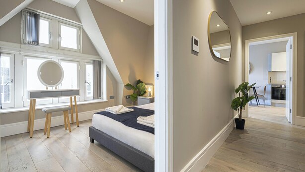 A bedroom with a bed, bedside table, and a large window. - Superb 2 Bedroom Apartments (London)