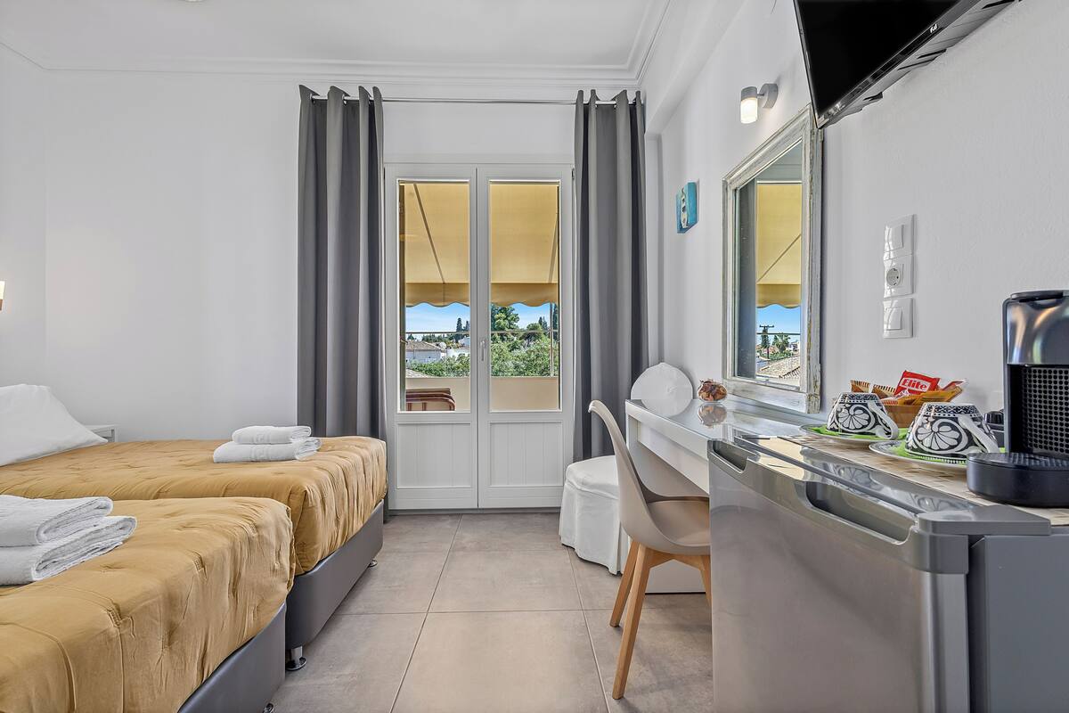 Habitación de hotel con dos camas, un escritorio, una silla, ventana con cortinas y vista a zonas verdes.