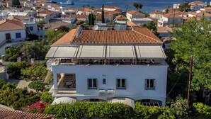 A coastal residential area with terracotta-tiled roofs, a white building with a balcony, and a view of the sea.
