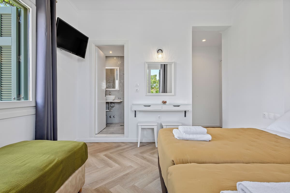 Habitación de hotel con cama, escritorio, espejo, televisión y baño visible a través de una puerta abierta.