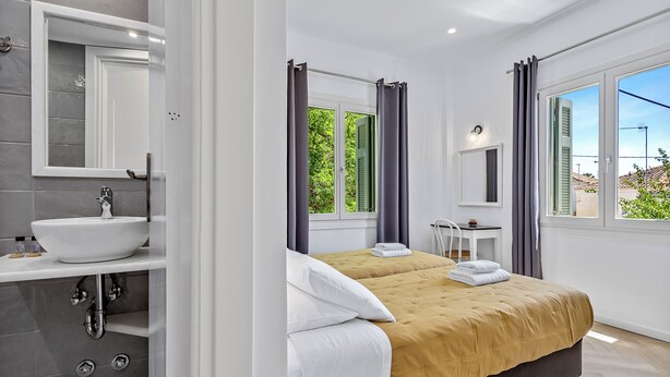 A modern hotel room with a large bed, a bathroom with a sink, and a window with curtains.