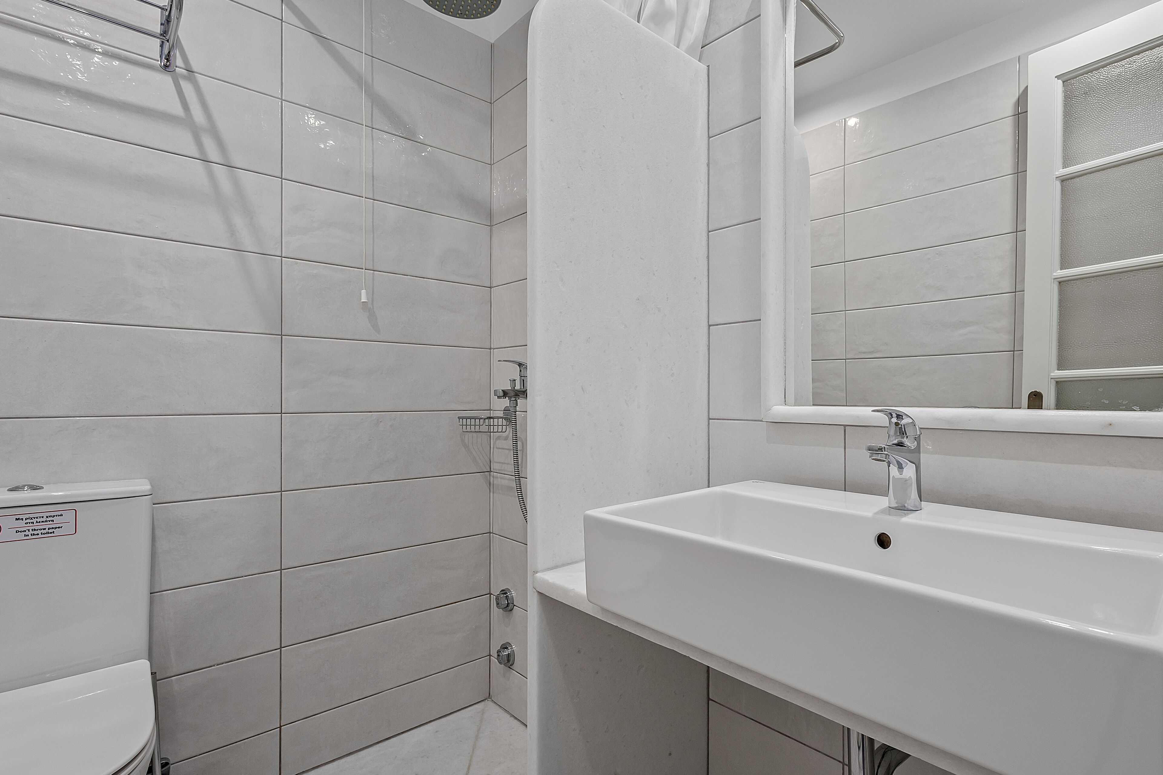 A modern bathroom with white tiles, a toilet, a sink, and a shower.