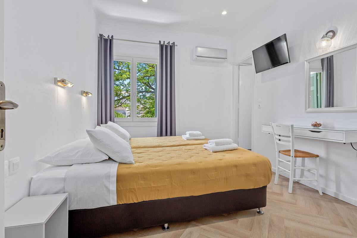 Habitación de hotel con cama, escritorio, silla, televisor y aire acondicionado.