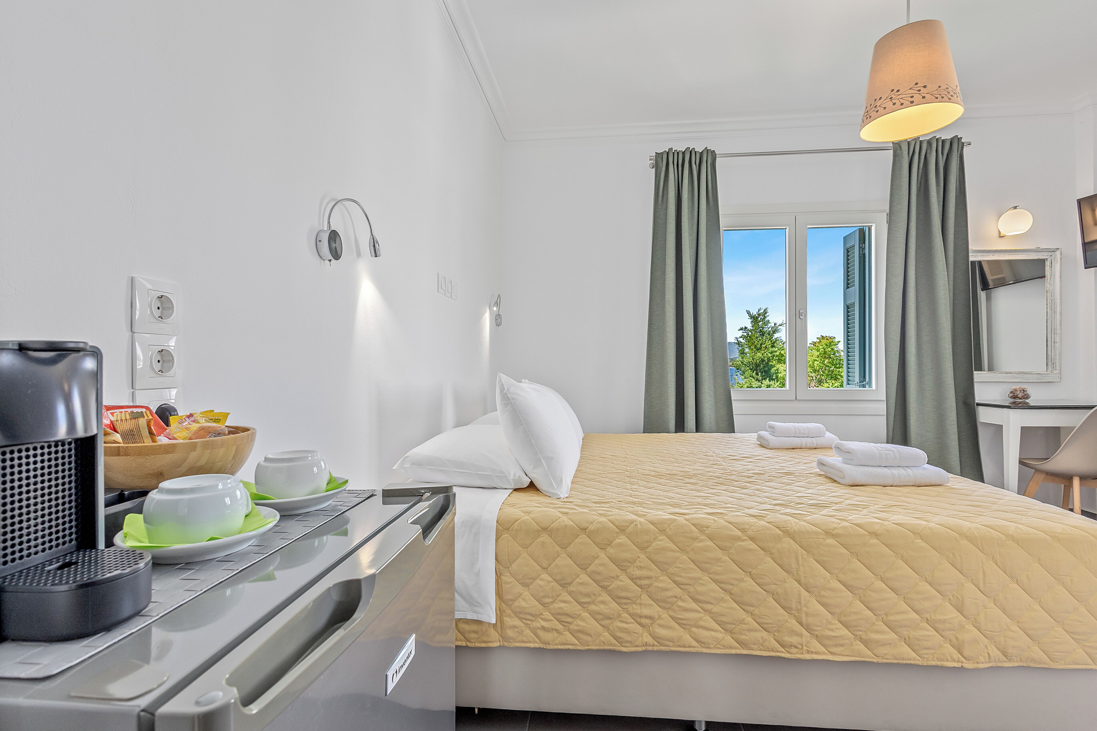 A hotel room with a bed, a desk, a coffee machine, and a window with curtains.