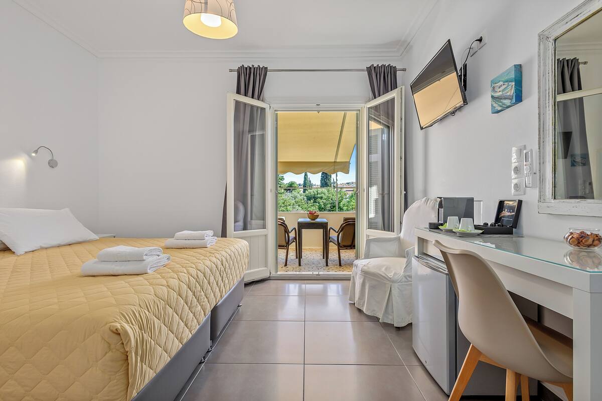 Habitación de hotel con cama, escritorio, silla, una pequeña mesa con sillas y balcón con mesa y sillas.