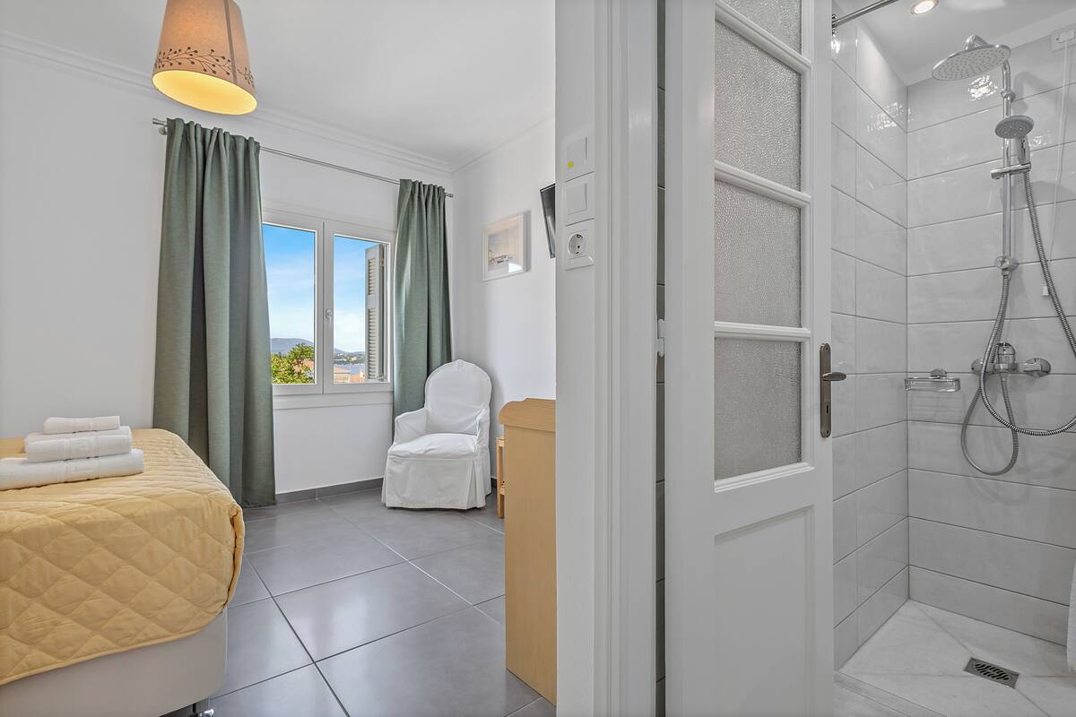 Habitación de hotel con cama, una silla, ducha y ventana con cortinas.