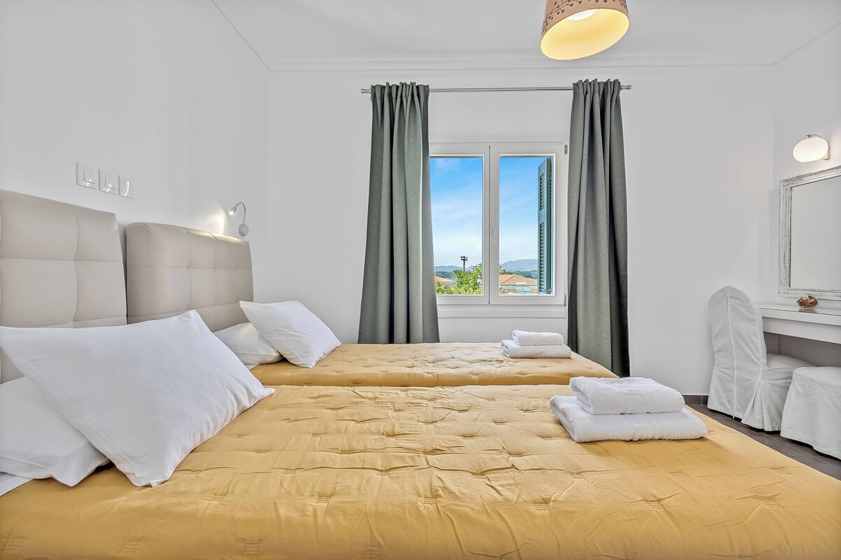Habitación de hotel con dos camas, un ventanal grande, un espejo y vistas a la ciudad.
