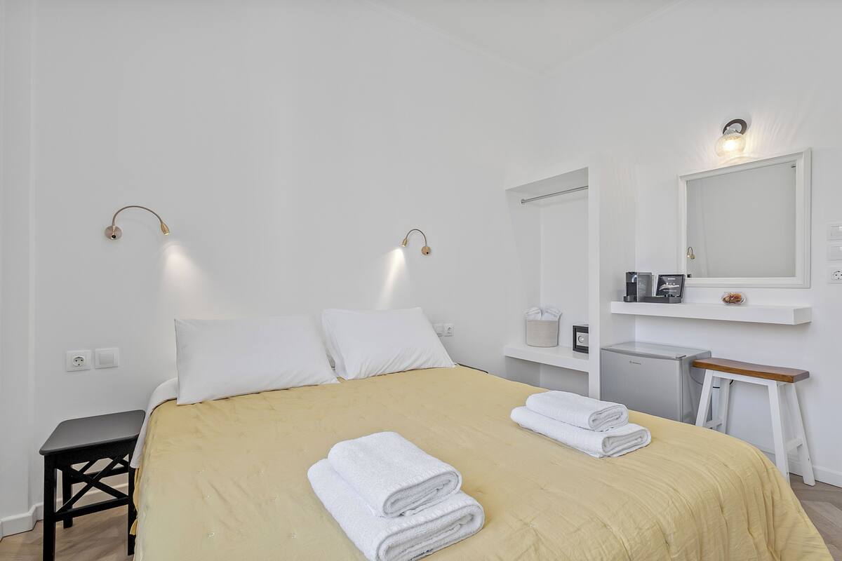 Una cama bien hecha con toallas blancas, una mesita de noche pequeña, un espejo montado en la pared y un enchufe.