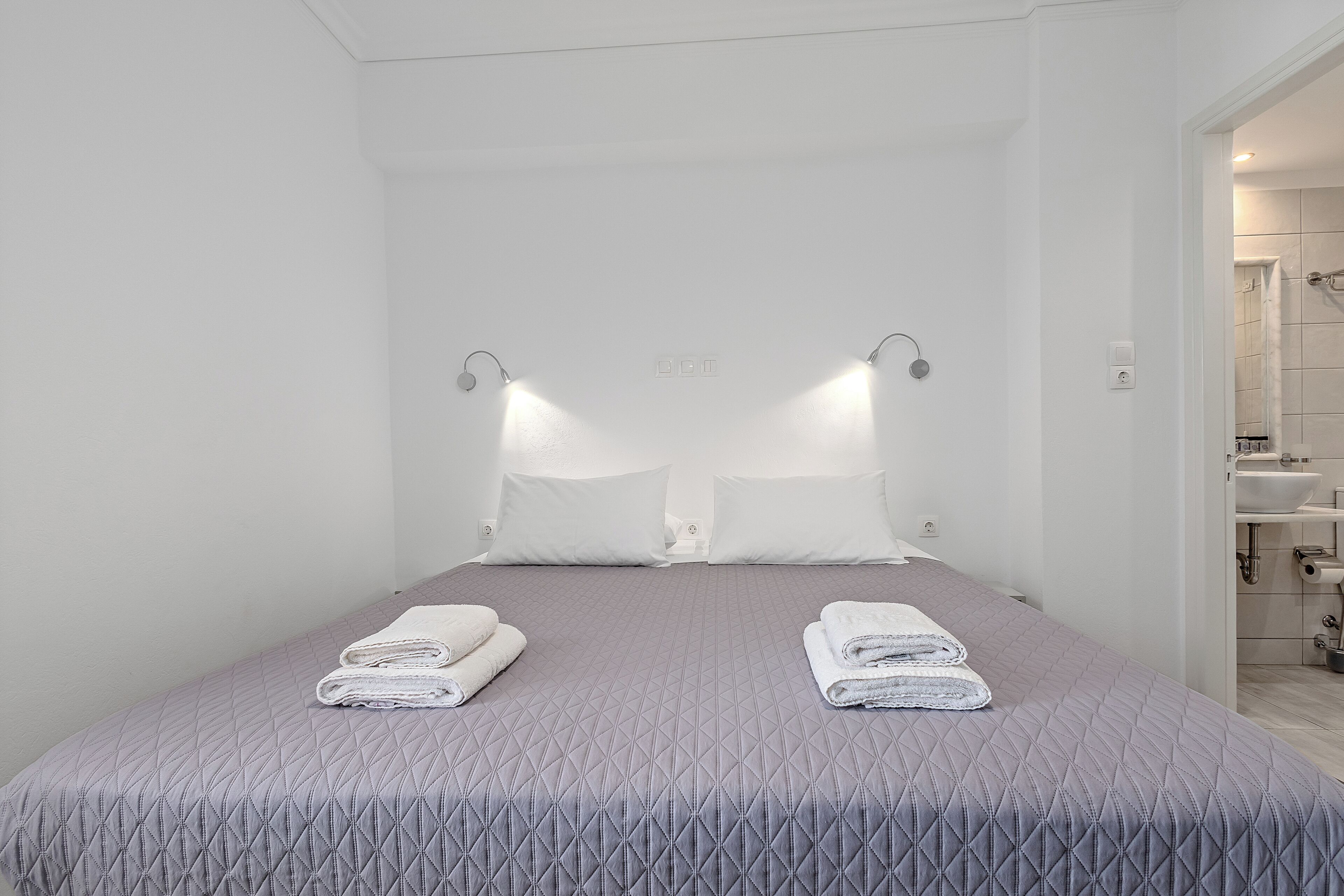 A hotel room with a bed, two pillows, a folded towel, and a nightstand.
