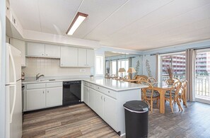 Eine moderne Küche mit weißen Schränken, einem Geschirrspüler und einem Essbereich mit Korbstühlen und einem Glastisch.
