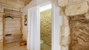 Een badkamer met een stenen muur, een ophangrek voor handdoeken, een mand en een toilet.