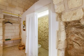 Ein Badezimmer mit Steinwand, einer hängenden Handtuchstange, einem Korb und einer Toilette.