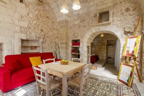 A stone-walled room with a red sofa, wooden dining table, and chairs. - A comfortable, open-plan apartment for two, featuring typical and charming stone architecture, located in Cannole, a quiet village in the heart of Salento. It sits in a courtyard just steps from the town center and Granafei Castle. It's within easy reach (Cannole)